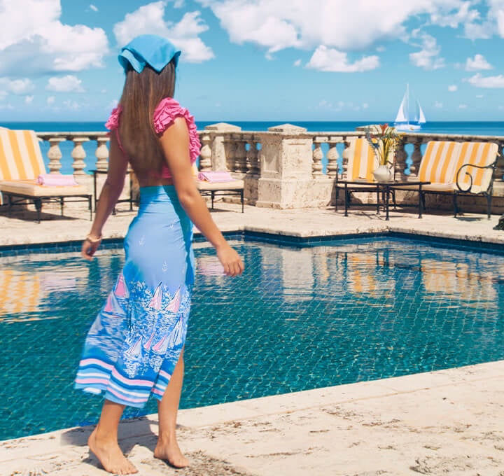 model by pool wearing pink bathingsuit and blue skirt