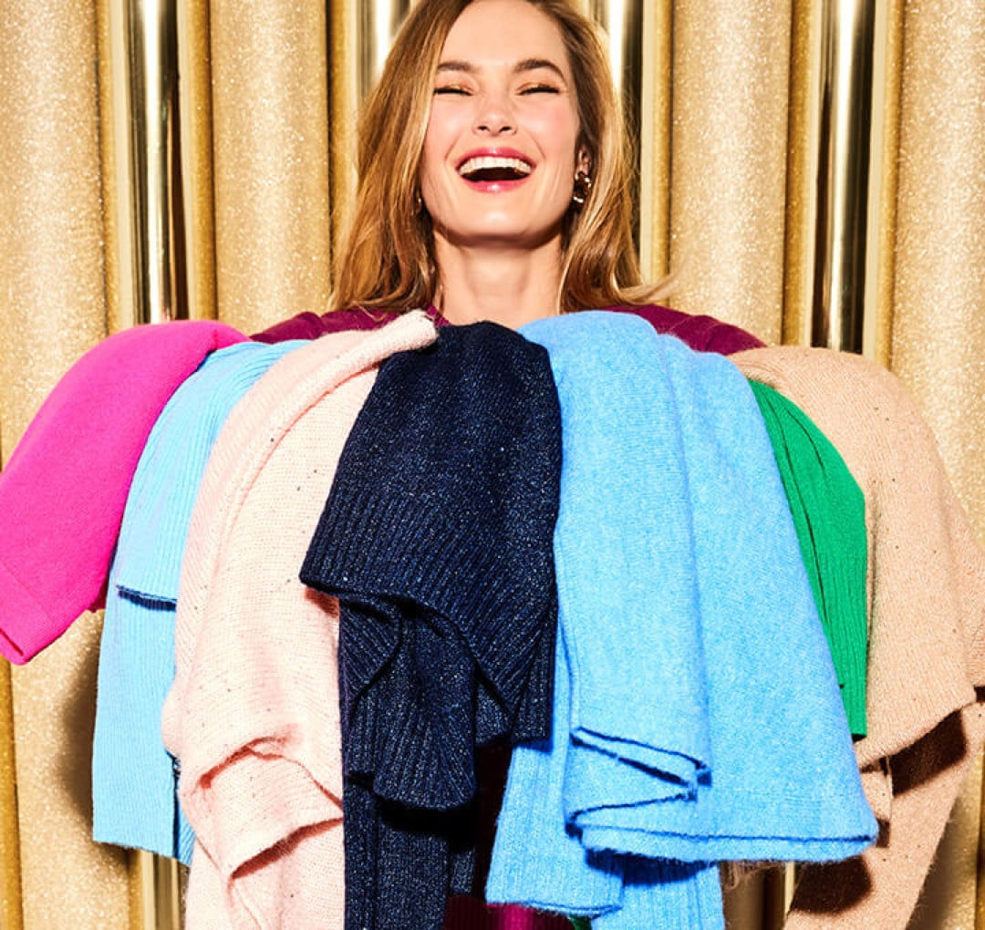 woman smiling holding sweaters