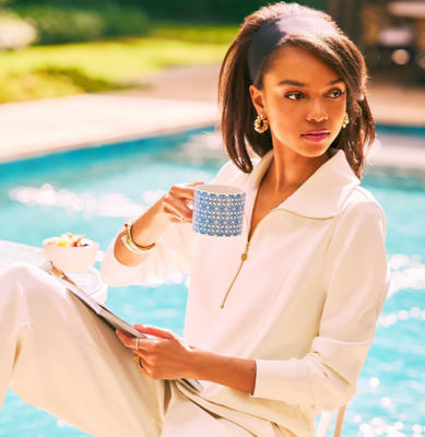 Woman wearing a cream half zip pullover top and holding a blue printed mug