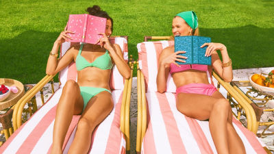 Two women in swimsuits laying on pool chairs