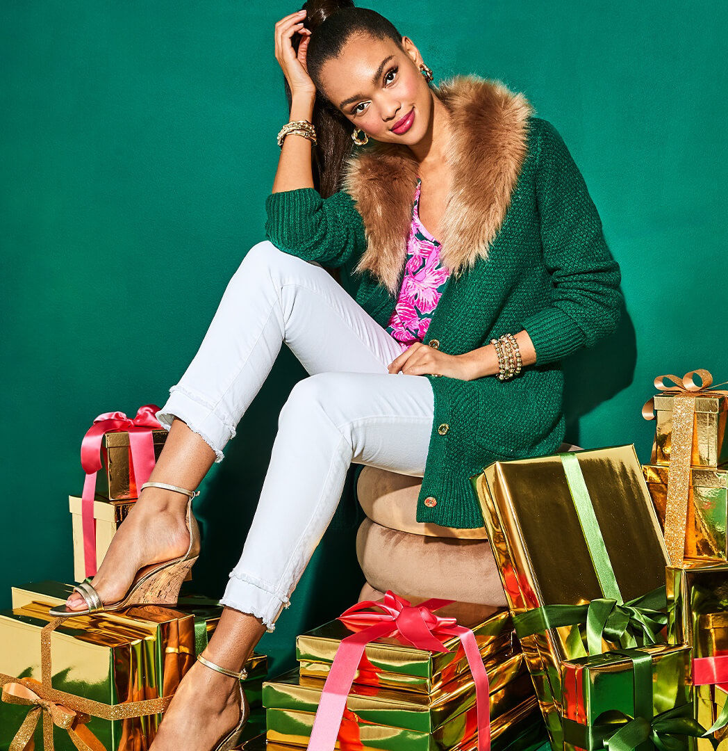 Woman wearing green cardigan with brown fur collar sitting on top of gifts