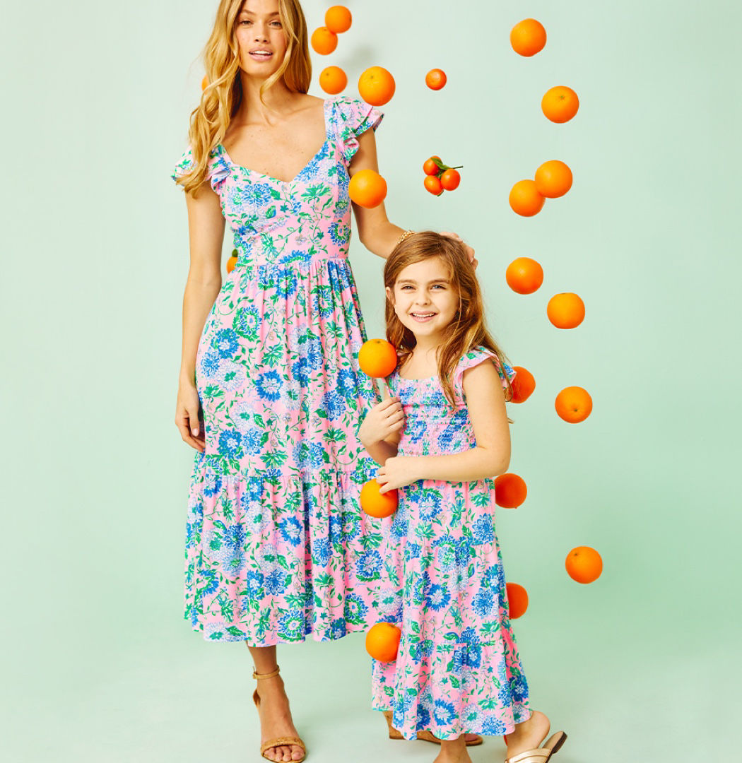 Mother and daughter wearing matching floral maxi dresses surrounded by oranges