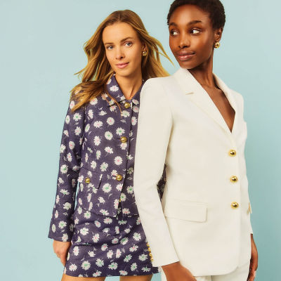 Woman wearing a navy pattern jacket and another woman wearing a white blazer and shorts